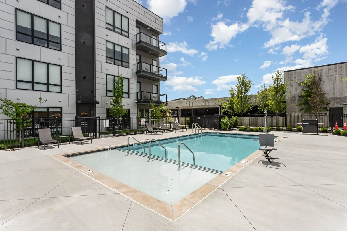 A beautifully landscaped outdoor pool area with lounge chairs, a visible balcony, and vibrant greenery. The clear blue water invites relaxation, while the setup suggests opportunities for sunbathing, swimming, and social gatherings.