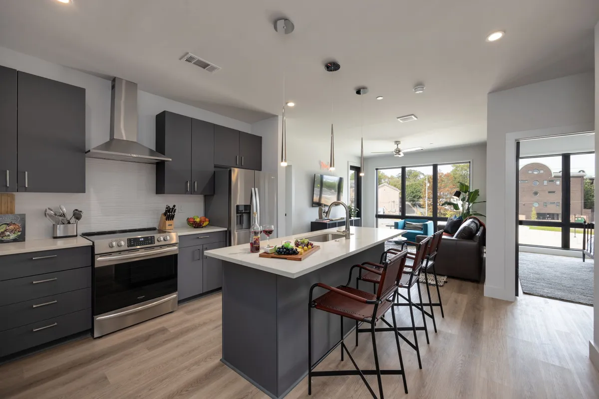 A modern kitchen interior featuring a central island, gleaming stainless steel appliances, expansive windows that let in natural light, and a seating area at the breakfast bar. The space is open and inviting, with clean lines and a contemporary design, ideal for both cooking and entertaining.