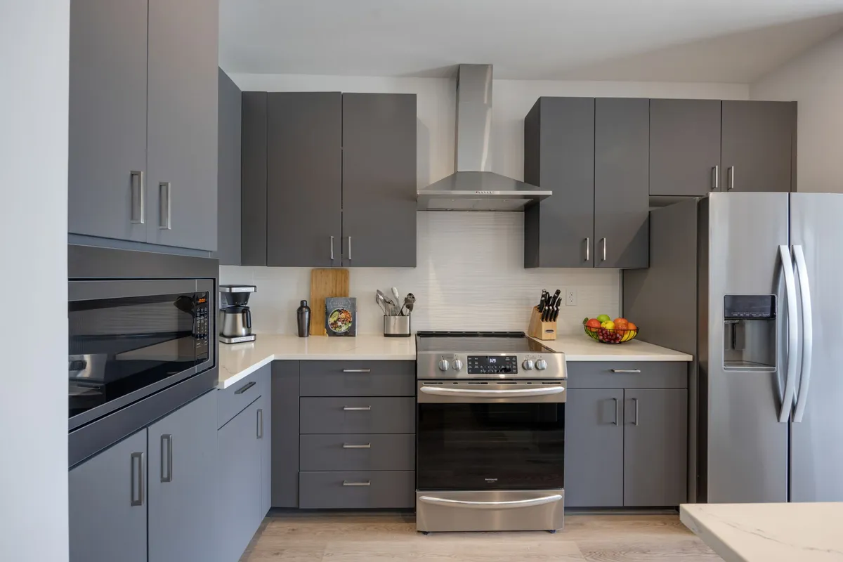 A stylish kitchen with dark cabinetry, gleaming stainless steel appliances, and a countertop adorned with a fruit bowl. The arrangement emphasizes functionality and contemporary design, making it suitable for both cooking enthusiasts and those seeking comfort.