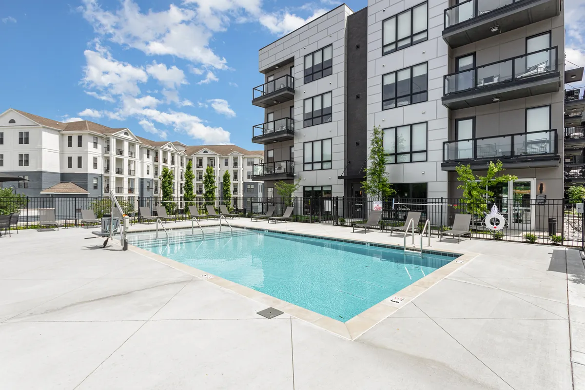 An exterior view of the swimming pool area with elegant balconies overhead and lush landscaping, capturing moments of swimming, sunbathing, and casual poolside gatherings. Sunset lighting adds a warm, resort-like ambience.